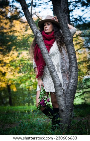 young woman wearing hat,  red wool scarf and wool dress  outdoor shot in wood hold flowers in hand full body shot