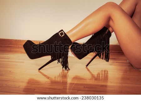 long slim woman legs in black ankle high heel fringe boot indoor shot on parquet against wall retro colors