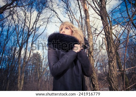 blonde woman in warm coat with fur in the forest, cold winter day