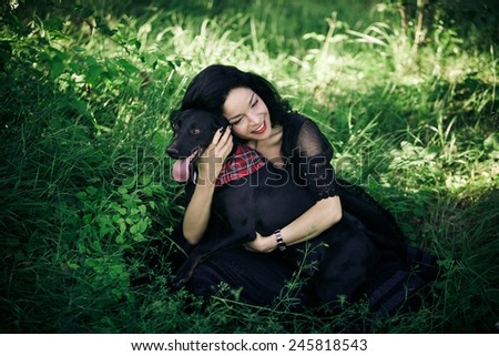 beautiful young woman in black elegant dress sit on grass field with her dog summer day