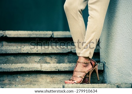 woman legs in high heel golden sandals stand on stairs, outdoor shot