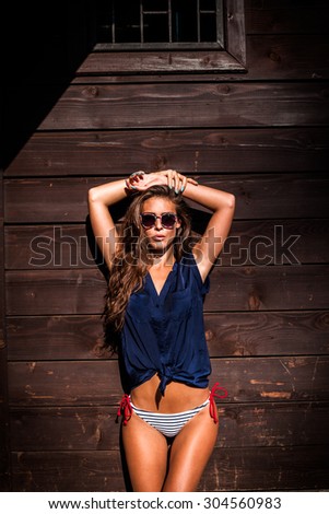 beautiful tanned young woman in bikini and navy blue summer shirt against wooden wall outdoor shot hot summer day