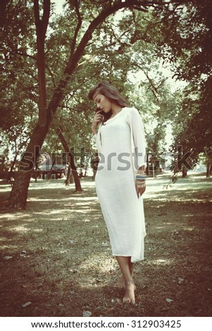 beautiful young barefoot woman in long linen white dress stand standing between trees full body shot, natural light