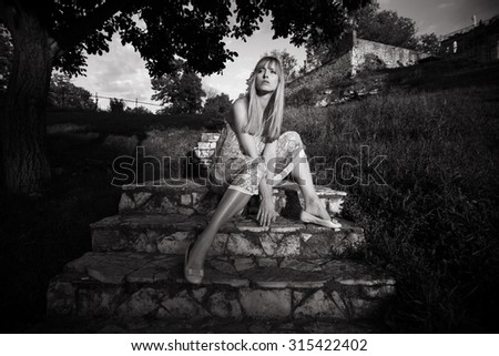 blond young woman sitting on the stairs in fashionable dress, full body shot, front view, outdoor shot, summer day at Kalemegdan, Belgrade