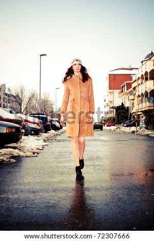 young woman wearing coat walking down the street, cold winter day