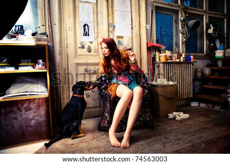 young woman wearing colorful clothes in art studio sit by the door with  her dog