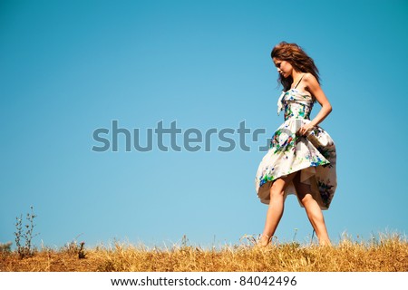 young woman in summer dress walk through the grass, blue sky in background, summer day