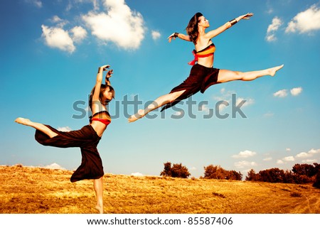 Women dance in summer field, sky with clouds in background, small amount of grain added