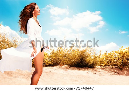 smiling woman in white dress and bikini standing on beach, sunny summer day