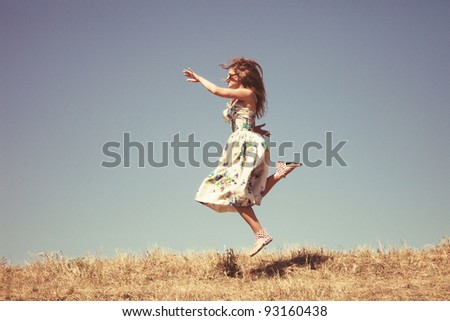 young woman in silk dress on top of the hill jumps, sky in background, retro colours, grain added