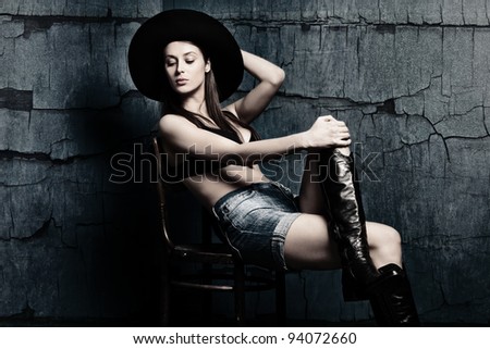 attractive woman in boots shorts and hat sit on chair in old grunge room