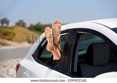 Women\'s legs sticking out the car window. The concept of relaxation and travel