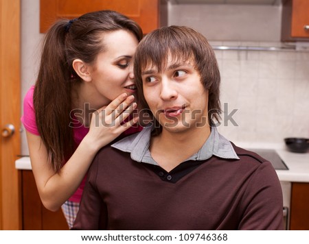 girl whispers on an ear to the guy in kitchen
