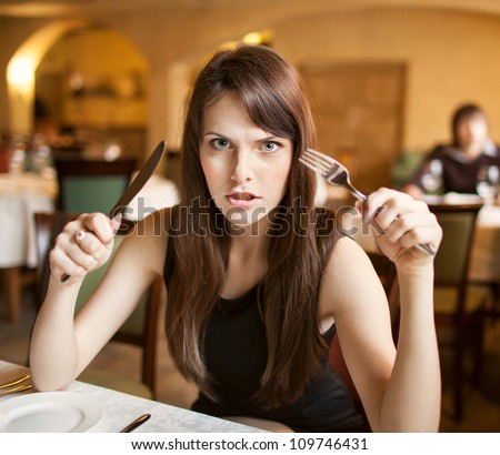 hungry and angry female person at restaurant holding fork and knife