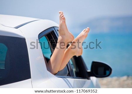 Concept of summer car trip vacation . Woman legs out the window in car at background of sea water
