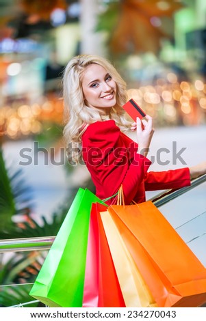 beautiful young woman holding colored shopping bags and credit card in the shopping mall on sales