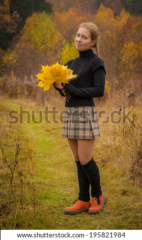 blonde girl in pleated skirt holds autumn leaves