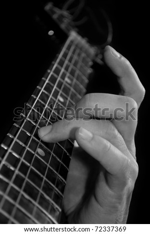 fingers on acoustic six-string guitar fretboard, black and white