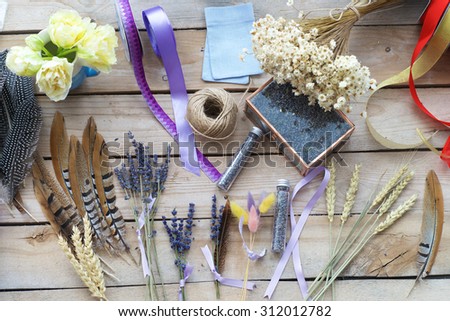 Flower decorating supplies including feathers, roses, baby\'s breath dried flowers, twine and ribbon on wooden plank background.