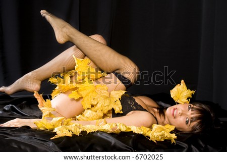 Very sexual woman lays on black silk linen with autumn leaves