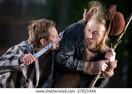 Two actors enacting a scene of a dangerous robber with a knife robbing a guy.