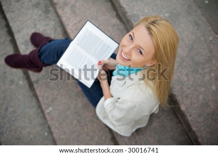 Young woman sits on stone steps, she looks upwards. In a lap opened book.