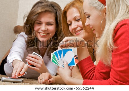 Three pretty girls lying on the floor, playing a game of cards UNO.