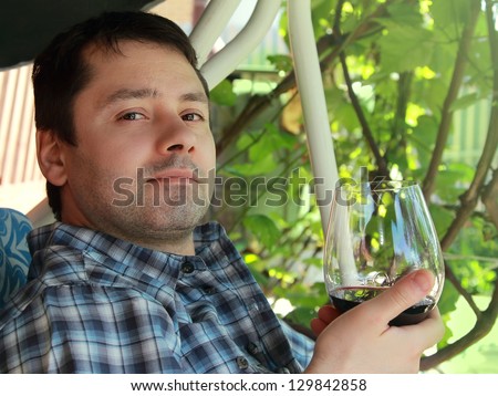 Young man drinking red wine outdoor background and looking calm. Closeup portrait