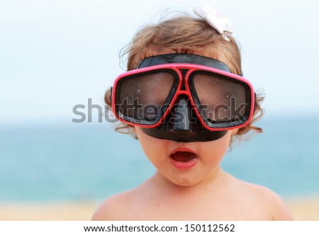 Surprising baby girl in diving mask looking fun on blue sea background