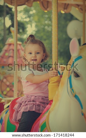 Happy smiling girl riding on horse on carousel outdoors summer background. Vintage portrait