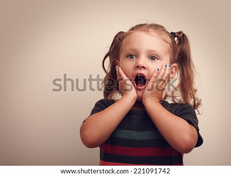 Cute surprising child girl with opened mouth and hand near the face looking on empty copy space. Vintage portrait