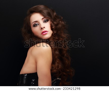 Beautiful makeup woman with brown long curly hair looking on black background. Bright pink lipstick and evening makeup