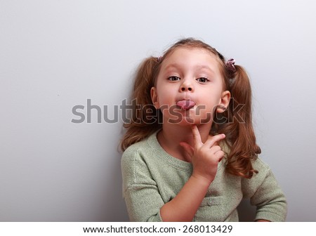 Thinking grimacing girl showing tongue with finger under face and looking funny in camera with empty copy space