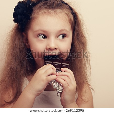 Happy surprising kid girl eating chocolate and looking with long hair style. Vintage closeup