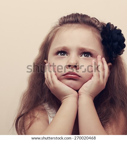 Lonely thinking about beautiful girl with sad eyes looking up with hands under face. Closeup vintage portrait