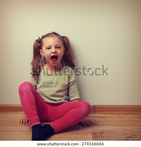 Happy crying kid with open mouth sitting on the floor in fashion clothes. Vintage color portrait