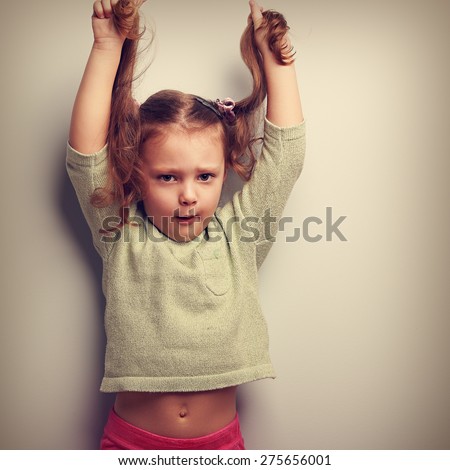 Active unhappy emotion kid girl pulling her long hair up. Vintage closeup portrait