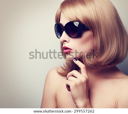 Female model profile in fashion sunglasses with blond short hair style and finger near face. Vintage closeup portrait