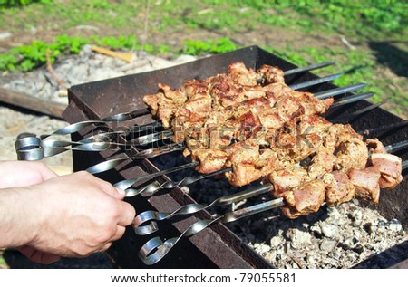 Man hands grilling tasty barbecue on black coals on mangal outdoor.