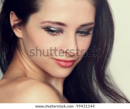 Closeup portrait of beautiful young woman with long hair, makeup attractive face and naked shoulders looking down