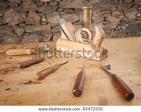 Carpentry tools spread on wooden table with stone wall in the background.