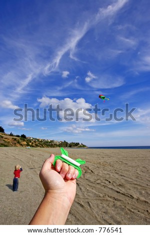 Person flying a kite on a sunny day at the beach with young son looking on