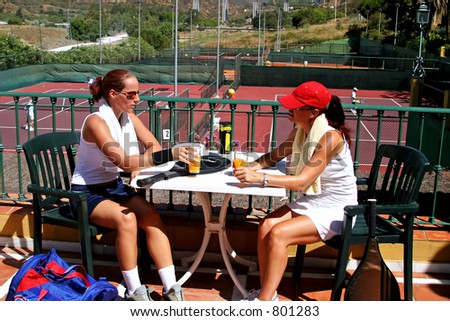 Two young attractive fit and healthy women enjoying a cold drink after a game of tennis in the sun whilst on vacation