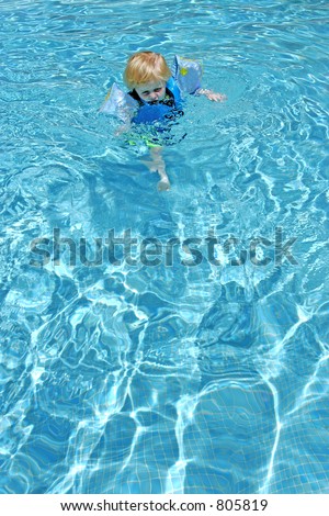 Young boy learning to swim in swimming pool with arm bands on while on vacation