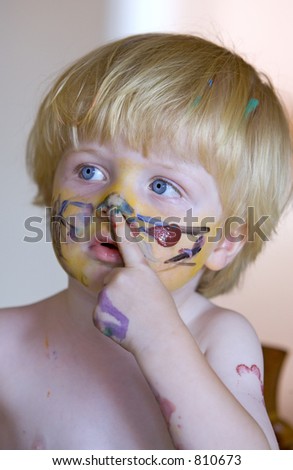 Close up of young boys face covered in colorful face paint and touching nose