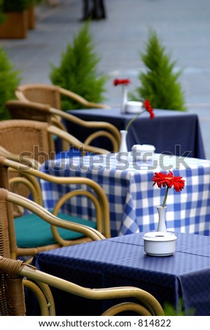 Empty tables with checkered table cloths on the street with roses on them outside a cafe bar or restaurant .