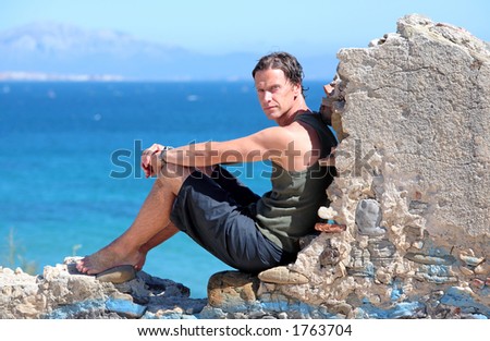 Handsome middle aged man sitting on an old stone wall in the sun