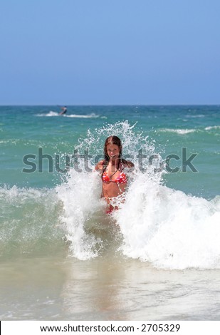 Sexy attractive young girl in red bikini being splashed by cold wave in the sea whilst on holiday or vacation