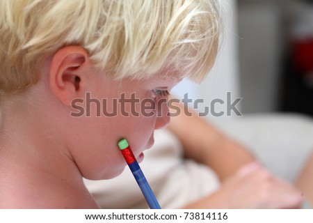 A young toddler or boy with light blonde hair concentrates on his homework with a blue pencil