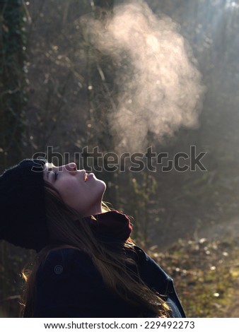 Beautiful girl breathing warm air during a cold autumn morning